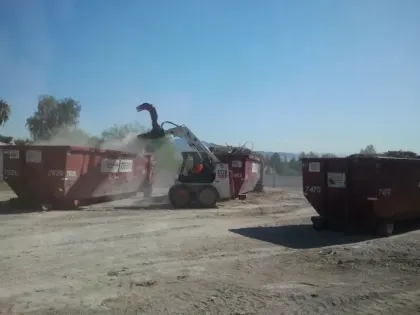 Skid-steer loader processing branches between roll-off dumpsters at a Las Vegas green-waste yard